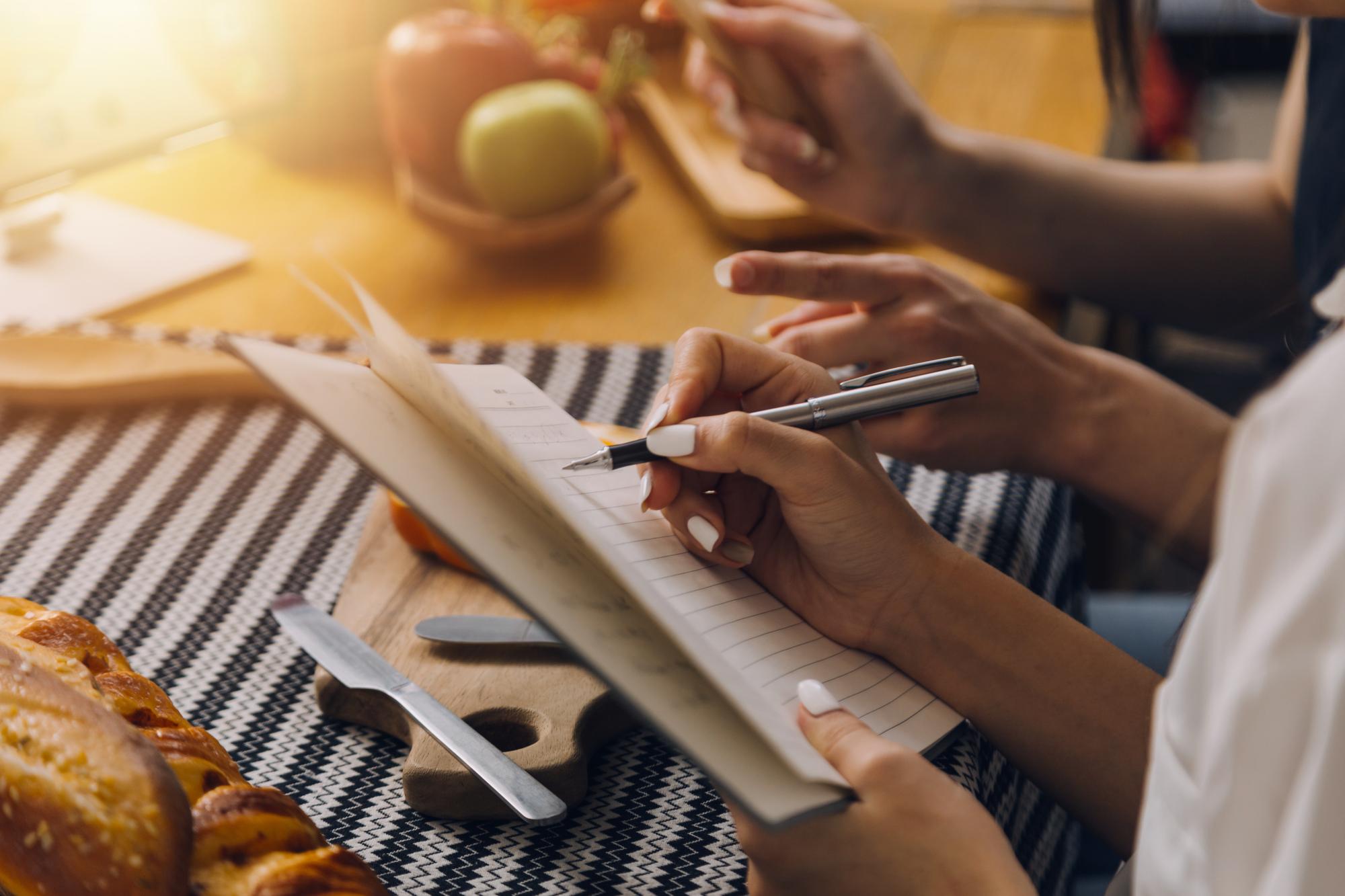 Köchin schreibt Rezeptnotizen in einem Notizbuch